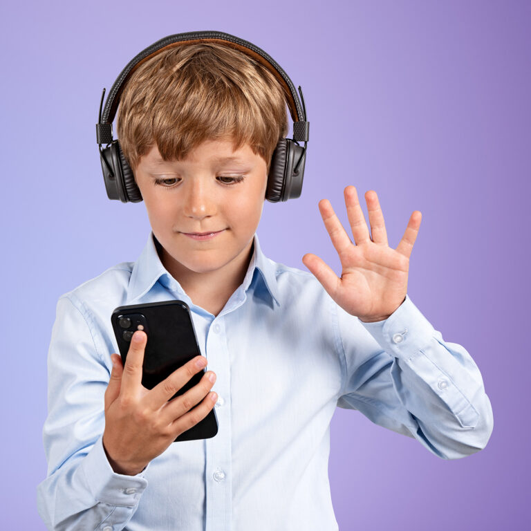 Handsome boy in formal wear raising hand with holding smartphone listening podcast in front of purple wall with copy space. Concept of internet learning, distant online education, progressive kids