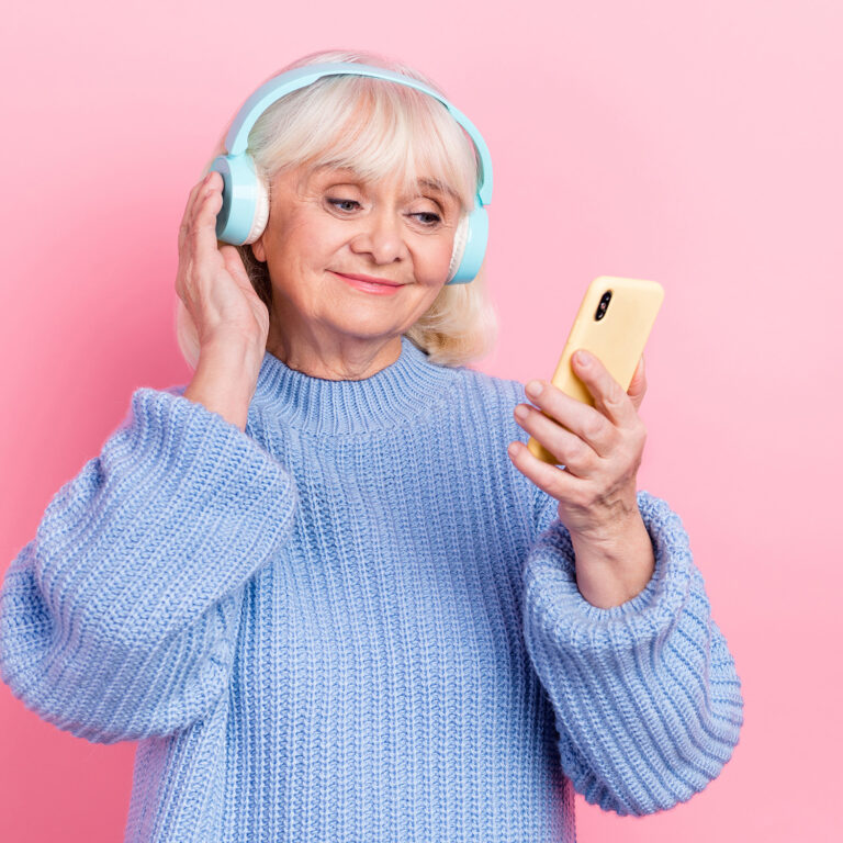 Portrait of attractive cheery focused grey-haired woman using device listening bass mp3 isolated over pink pastel color background.